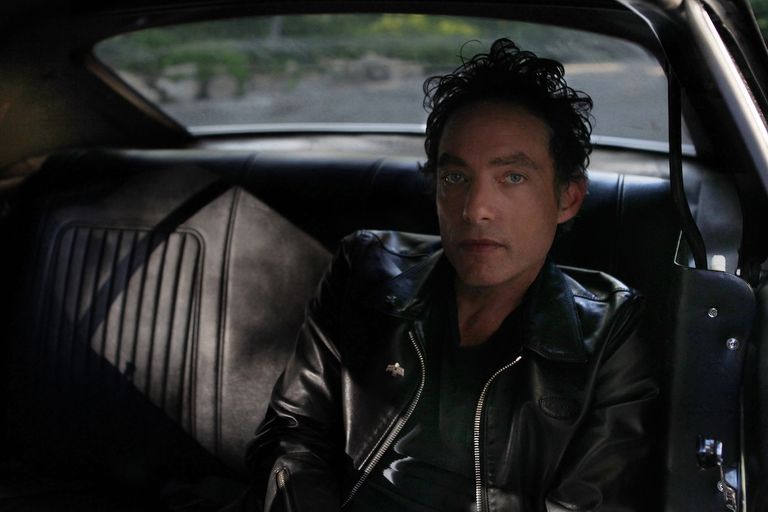 Jakob Dylan of rock band The Wallflowers wearing a leather jacket while sitting in the back seat of a car.